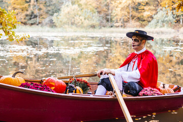 Obraz premium young man dressed as gondolier in gondola boat decorated with pumpkins on pond in autumn park celebrates Halloween and having fun, concept of Halloween carnival or costume party