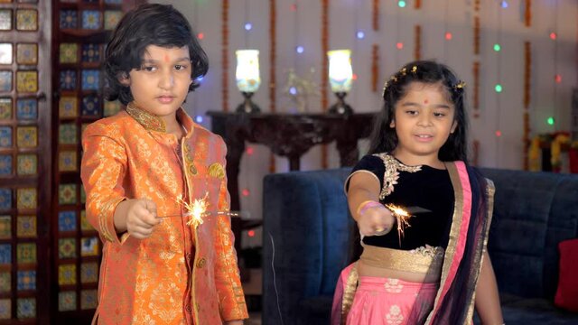 Young Indian brother-sister burning firecrackers / Phuljhadis together at home - Diwali celebrations. Adorable siblings in ethnic wear celebrating a Hindu festival together - an auspicious occasion...