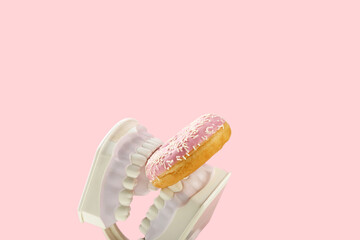 Plastic jaws hold sweet pink donut in teeth. Dental health, dentistry and caries concept. Colored...