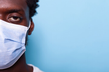 Close up of eye of young man with face mask for coronavirus protection while looking at camera. Face of casual person with mask for healthcare, standing over isolated background