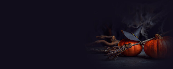 Mystical background of a witch. A decorative Halloween photo with a hat, pumpkins, spider webs and a broom. Background in black and orange colors close-up. 
