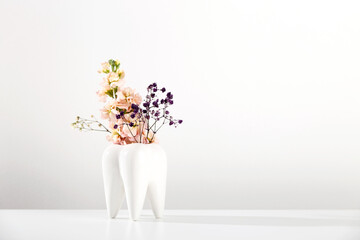 White big tooth vase with flowers on white background. Work and orthodontist dentist aesthetics....