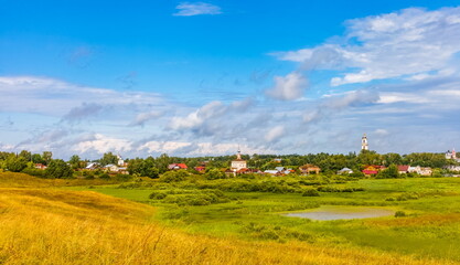 Fototapeta na wymiar Summer landscape with buildings, churches, trees, shrubs, grass, sky with clouds of the city of Suzdal in Russia
