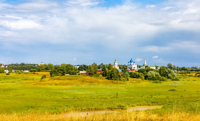 Summer landscape with buildings, churches, trees, shrubs, grass, sky with clouds of the city of Suzdal in Russia