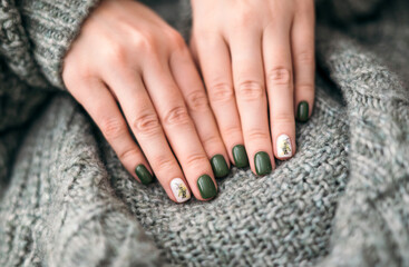 Women's hands with stylish green autumn manicure, against the background of a warm knitted plaid....