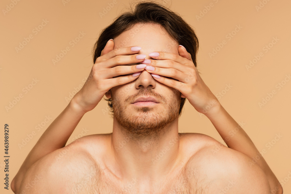 Wall mural woman covering eyes of young shirtless man isolated on beige.