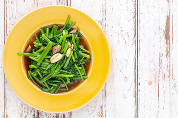 stir fried water spinach with garlic in yellow ceramic plate on white old wood texture background with copy space for text, top view, light and airy food photography, morning glory