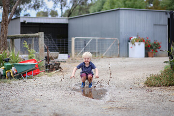Little boy wearing gum boots jumping and splashing in puddle