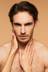 Obraz premium sexy man looking at camera near hands of woman seducing him isolated on beige.