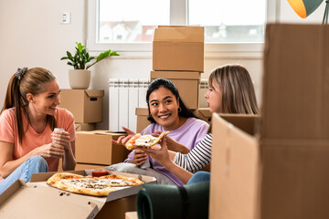 Female friends friends eating pizza after bringing the boxes into the new apartment. - obrazy, fototapety, plakaty