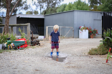 Little boy wearing gum boots jumping and splashing in puddle