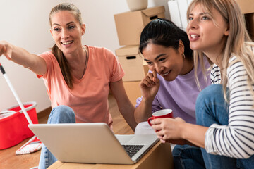 Female friends sitting on floor at new apartment using laptop.
