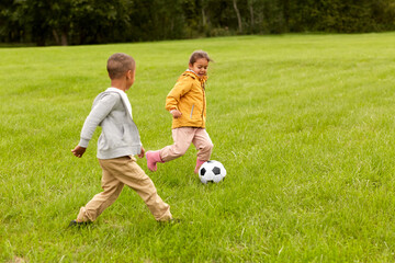 childhood, leisure games and people concept - happy little boy and girl with ball playing soccer at summer park