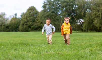 childhood, leisure and people concept - happy little boys running on green field at park