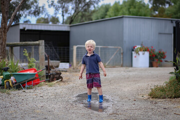 Little boy wearing gum boots jumping and splashing in puddle