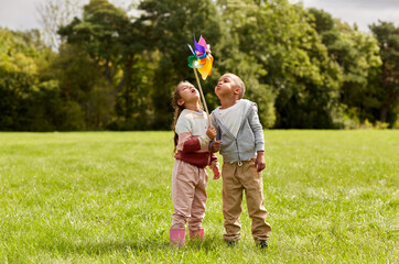 childhood, leisure and people concept - happy kids with pinwheel having fun at park