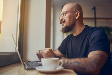 Focused hipster millennial man works at laptop while sitting in cafe with coffee. Freelance concept