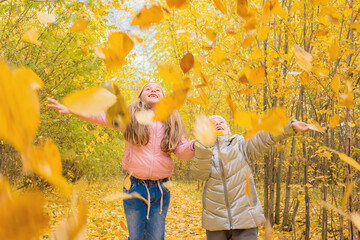 Two little girls are walking in the city park and catching falling yellow leaves with their hands. Happy childhood, joyful children