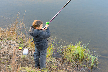 A child boy of six years old fishing on a fishing rod on the bank of the river in an autumn da