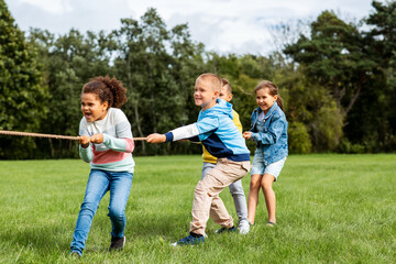 childhood, leisure and people concept - group of happy kids playing tug-of-war game and running at park