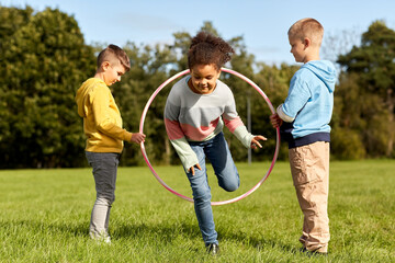 childhood, leisure and people concept - group of happy children playing game with hula hoop at park
