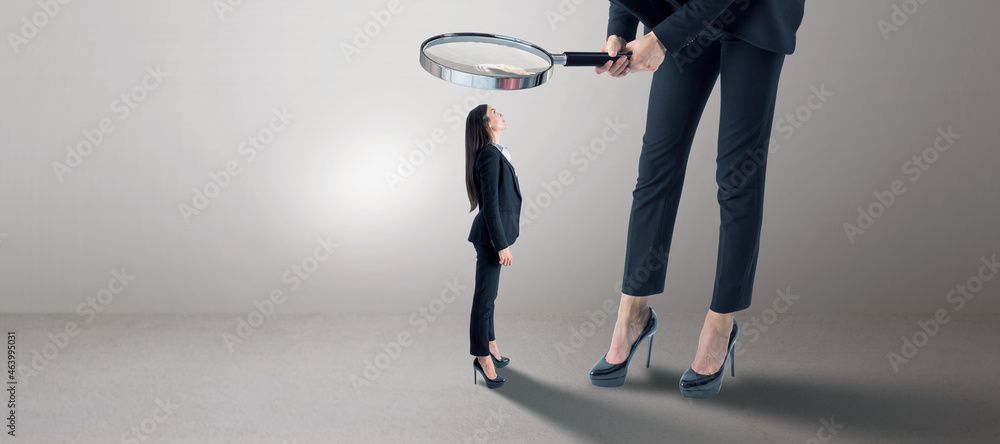 Poster Woman in suit using magnifier magnifying glass to look at tiny subordinate on concrete background with shadow and mock up place. Hiring and dominance concept.