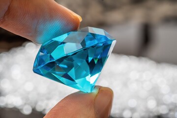 Hand is holding brilliant or diamond gem on black background.