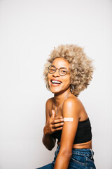 Portrait of a Young black latin woman showing the band-aid on her arm after vaccination standing...