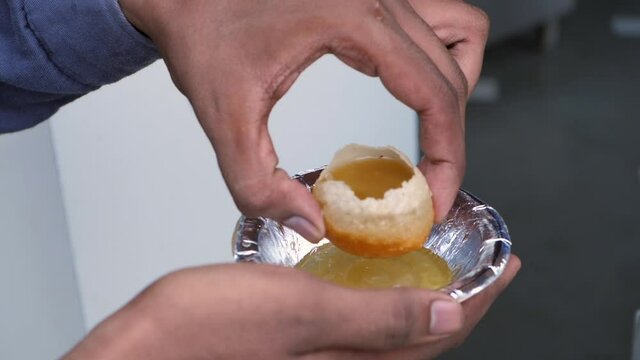 A North-Indian traditional food / Golgappe breaking into pieces on a paper plate. A man in casual clothes enjoying eating crispy Panipuri - a popular snack  street food  tasty dish