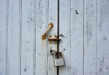 chipped white slat wood door with deadbolt, closed padlock and rusty handle