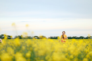 Pretty long haired girl playing in vibrant canola field in full bloom during Spring season