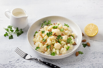 Cauliflower salad with apples, almonds, herbs and yogurt dressing on light gray textured background. Healthy homemade diet food
