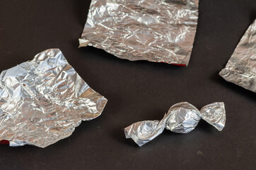 Round chocolate candy and empty wrappers on a black background.