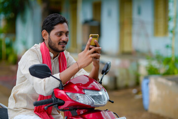 Indian farmer sitting on bike and using smartphone