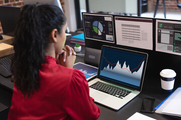 Biracial businesswoman sitting at desk using laptop with statistical data on screen