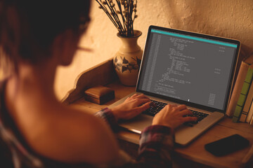 Back view of caucasian female programmer sitting at desk, using laptop with coding on screen