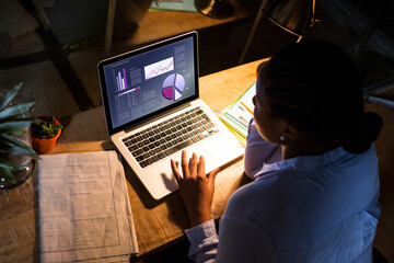 Biracial businesswoman sitting at desk using laptop with statistical data on screen