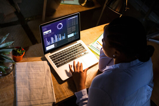 Biracial businesswoman sitting at desk using laptop with statistical data on screen