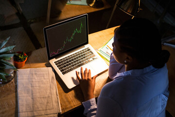 Biracial businesswoman sitting at desk, using laptop with statistical data on screen
