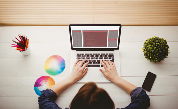 Caucasian female programmer sitting at desk with color charts, using laptop with coding on screen