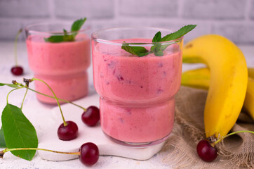 Cherry banana smoothies in glasses and fresh cherry bananas on a white wooden background.