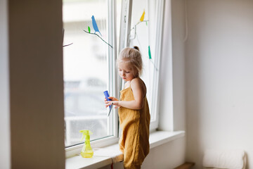 Cute caucasian girl toddler washes the window in a bright room, children's development center, montessori pedagogy and help with the housework