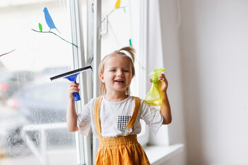 Cute caucasian girl toddler washes the window in a bright room, children's development center, montessori pedagogy and help with the housework
