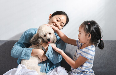 Young beautiful mother and little cute daughter have fun playing with dogs on the home sofa. Image of happy girl with dog mother relaxing at home. Happy family with pet friendship and care concept