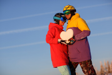 A young couple with a snowy heart in their hands against the background of a winter landscape in the ski resort.