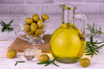 Olive oil in glass gravel fresh olives and rosemary on a white background.