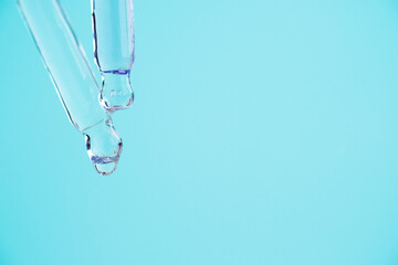 Transparent glass pipettes with a serum liquid dripping on blue background.