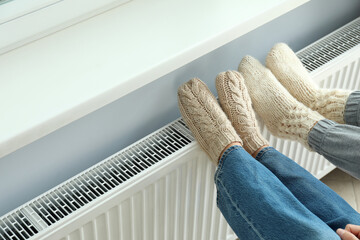 Concept of heating season with legs in knitted boots on radiator
