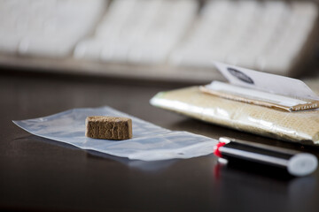 portion of hashish on plastic bag, with lighter and packet of tobacco in the background