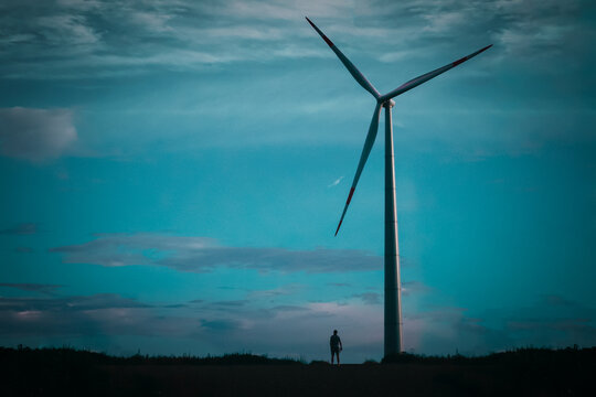 A wind turbine against a dark sky, a small silhouette of a man next to it